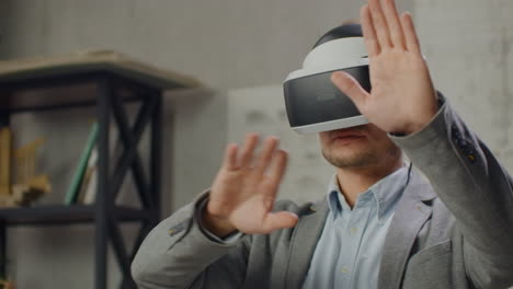 Modern-man-engineer-designer-in-the-office-with-large-windows-stands-in-a-virtual-reality-helmet-uses-gestures-to-manage-the-project-without-leaving-the-office.-Construction-control.-Design-project-of-the-building-and-interior.